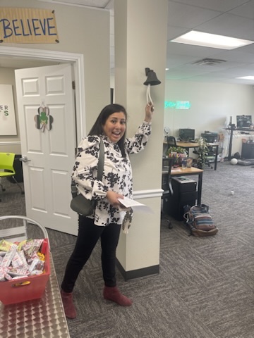 A Benefits Boss advisor ringing the office sales bell under the Believe sign