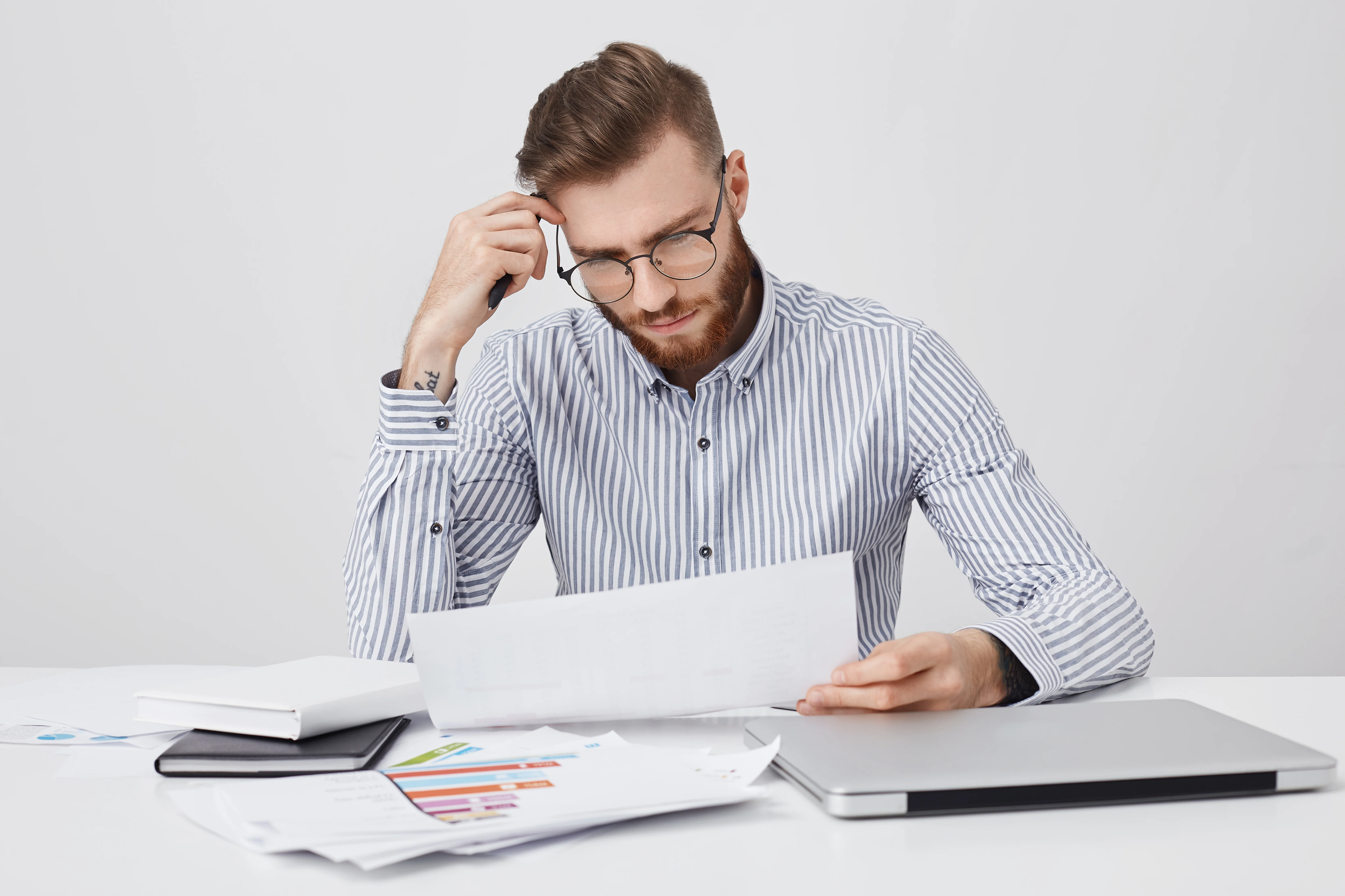 bearded man in glasses reading insurance document with concentrated expression at desk