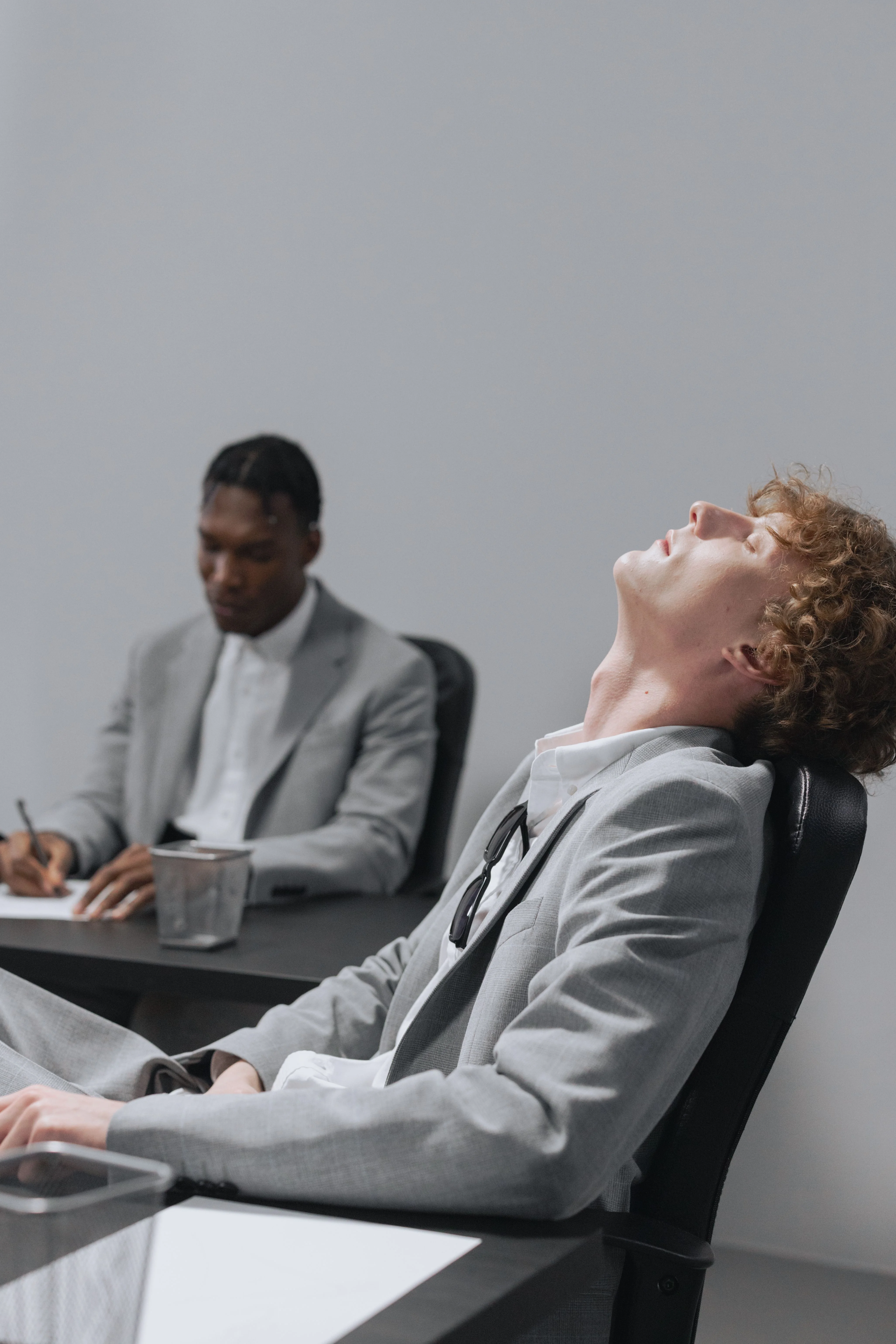 close up of anxious man in grey suit with eyes closed laying back in chair after getting laid off