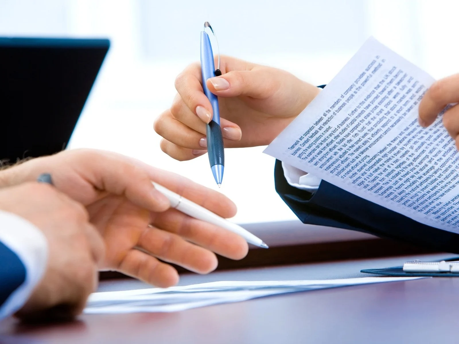 Close up of hands with pens reviewing printed contract document at desk
