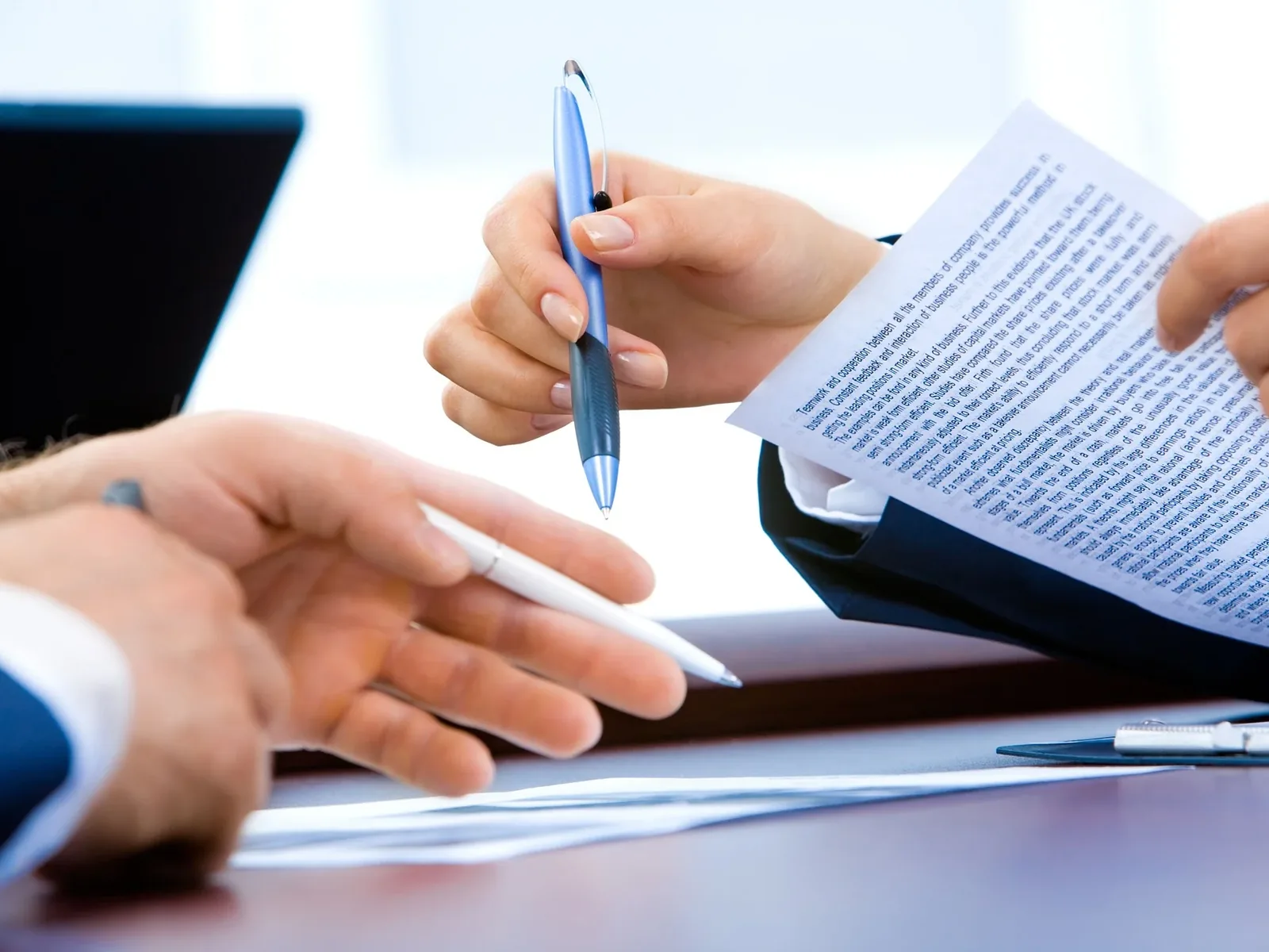 Close up of hands with pens reviewing printed contract document at desk