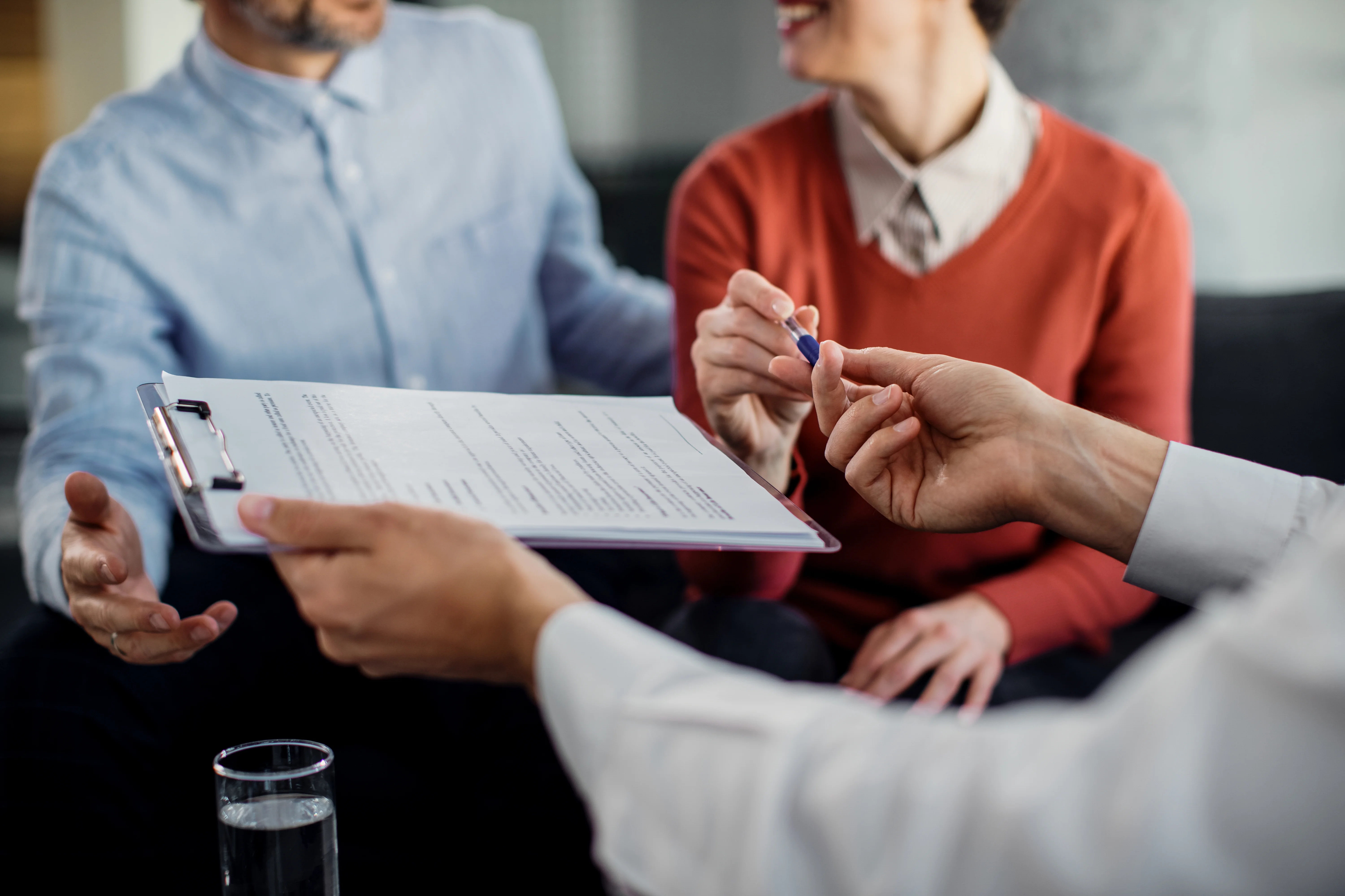 close up of insurance broker handing client pen to sign paperwork (1)