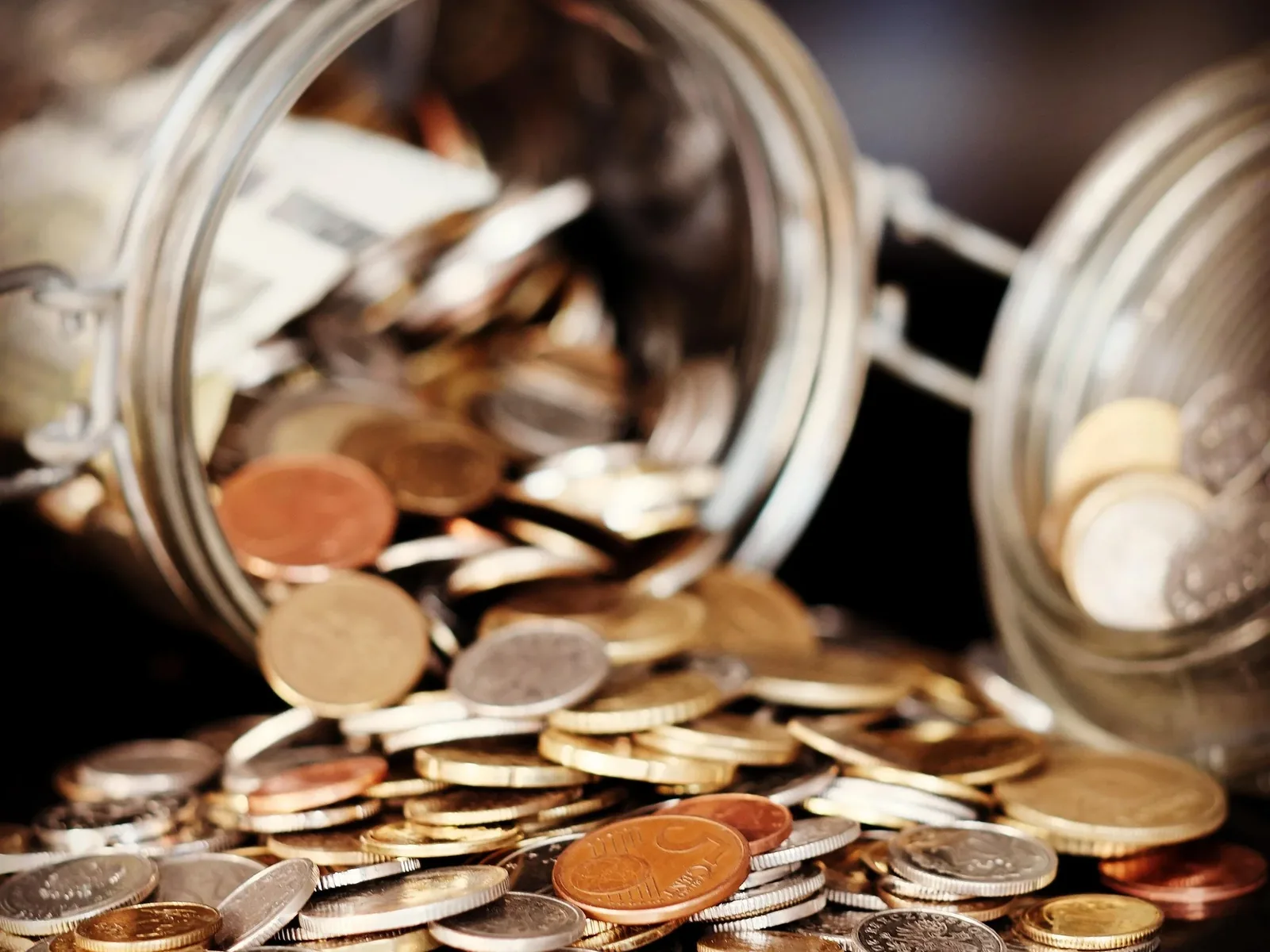 Coins spilling out of overturned glass savings jar