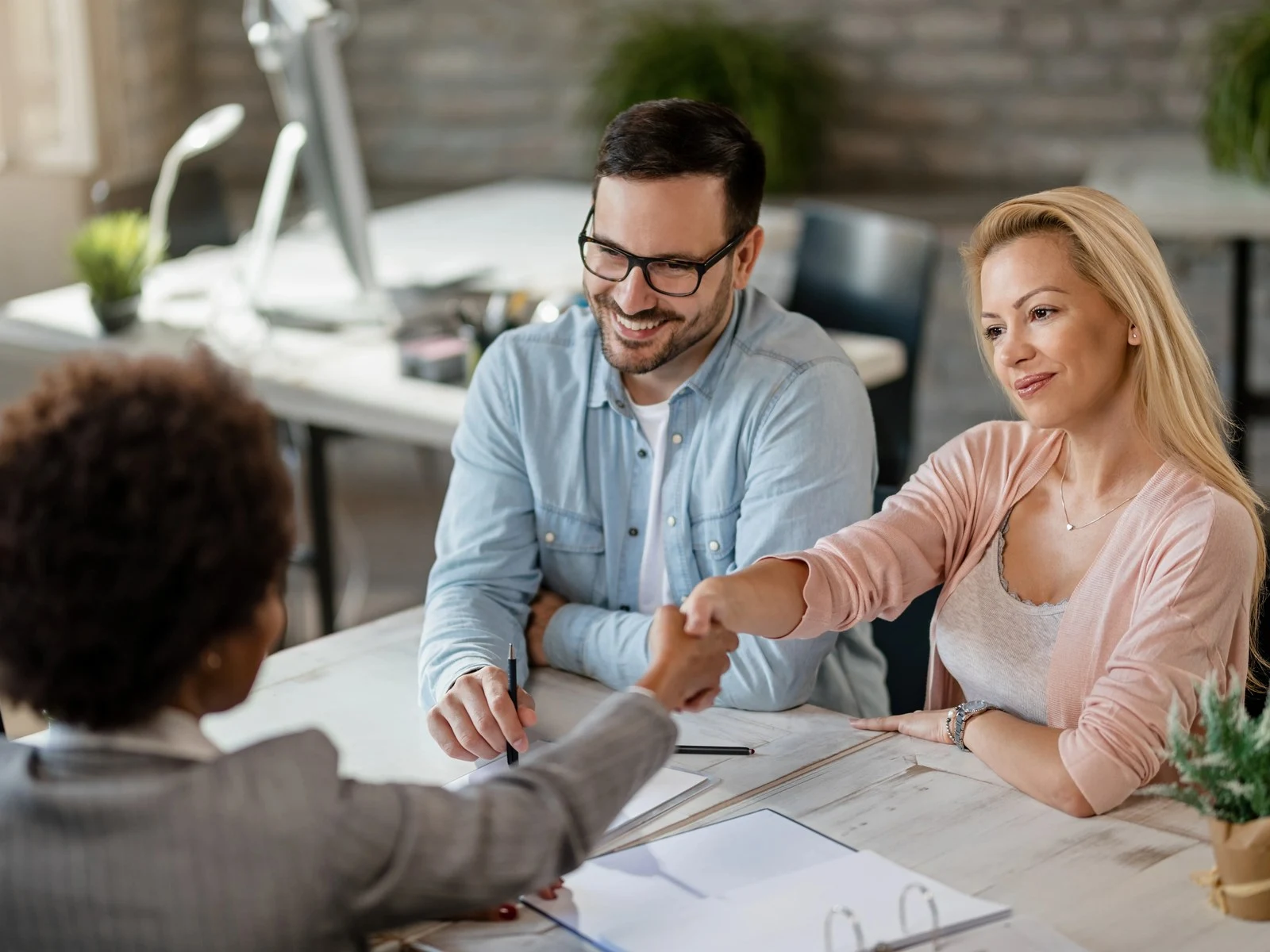 Couple shaking hands with advisor after reaching agreement in office