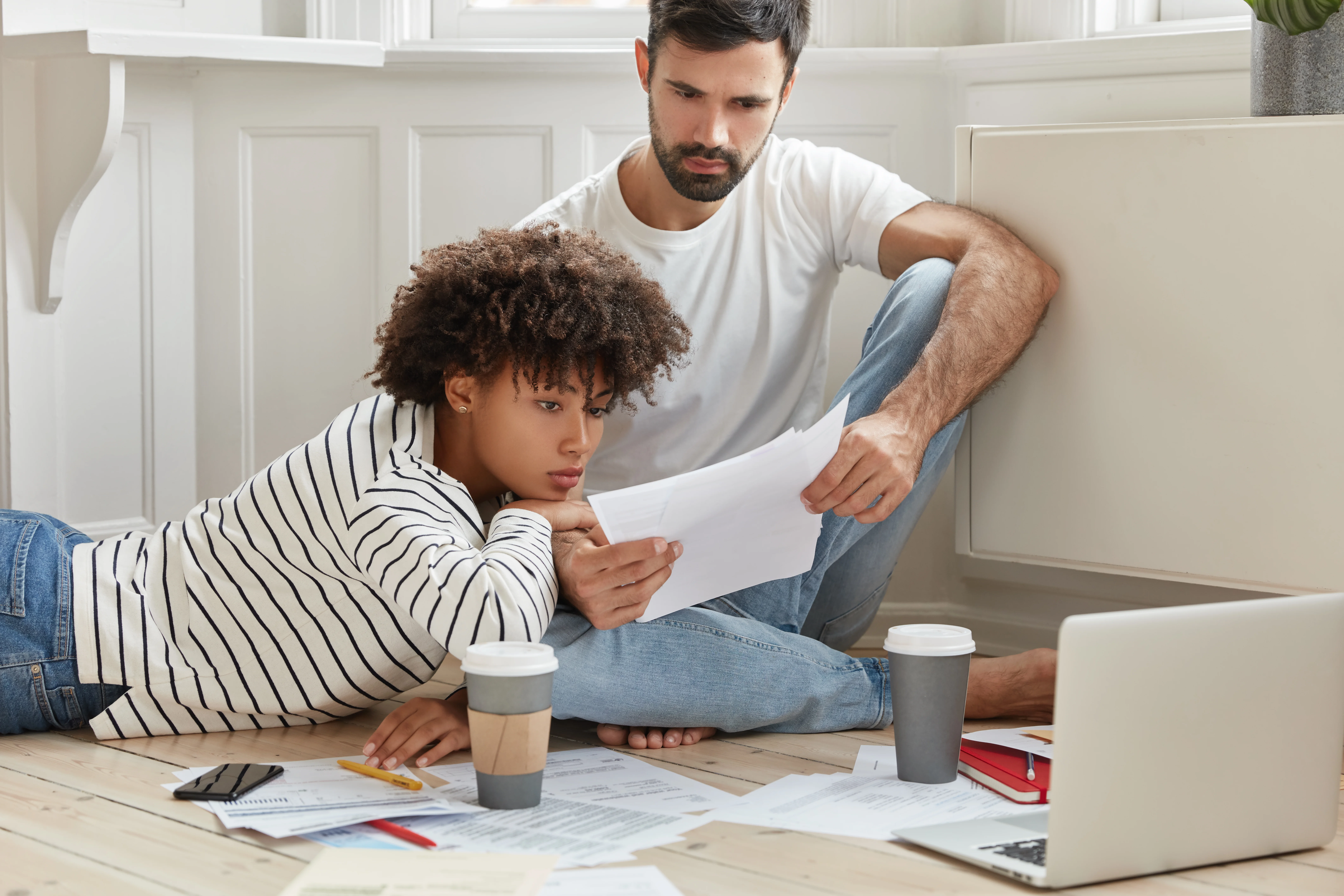 Couple sitting on kitchen floor with coffee analyzing insurance paperwork