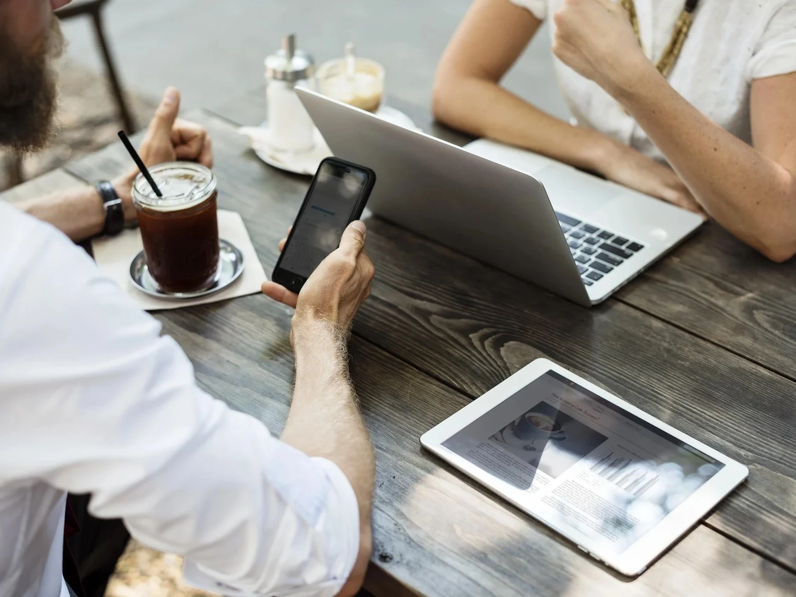 Coworkers at cafe table with laptop smartphone tablet and iced coffee