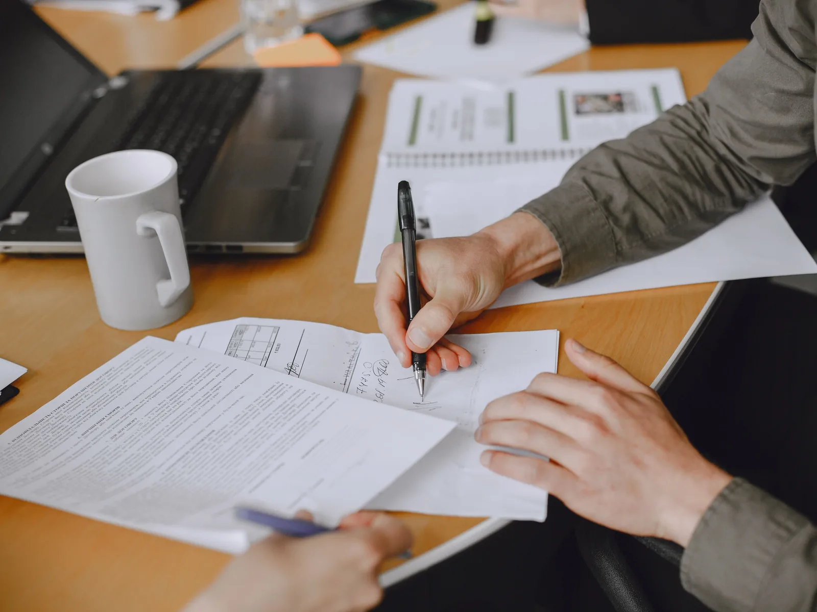 Hand signing document at office table with laptop and coffee mug