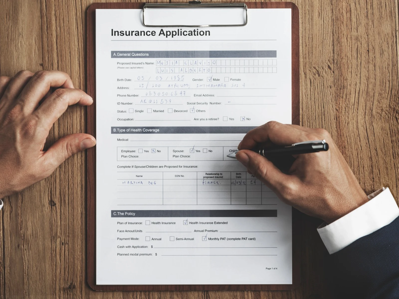 Hands filling out health insurance application form on clipboard at wooden desk