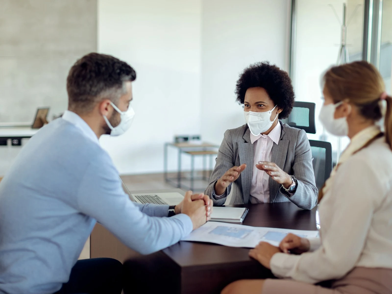 Insurance agent wearing face mask explaining coverage options to couple in office