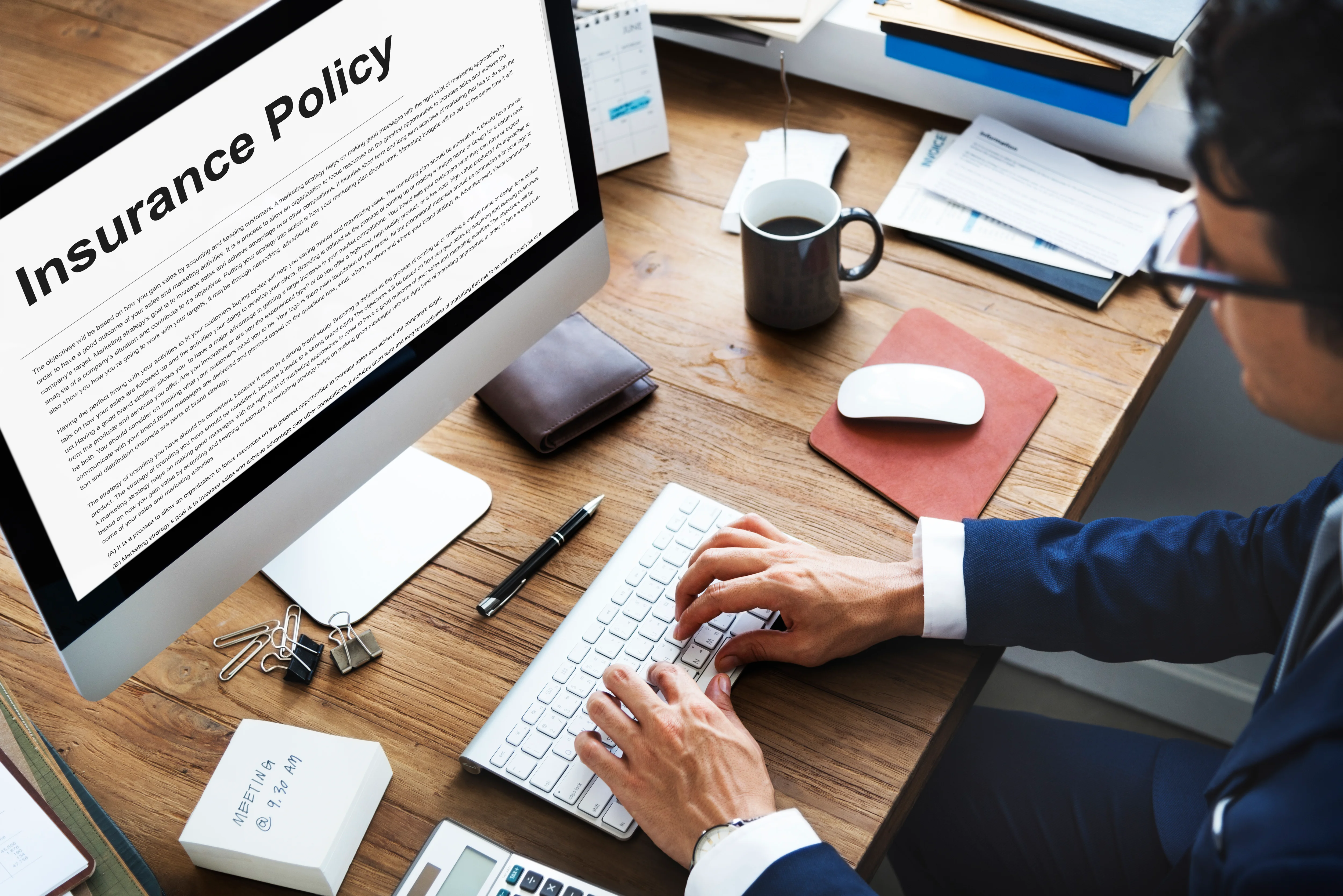 man typing at desk with insurance policy document on computer monitor