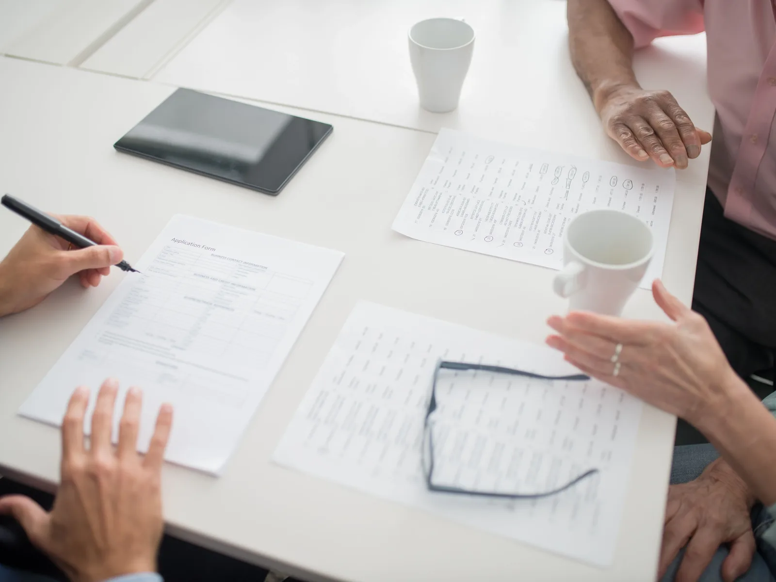 People reviewing application form and paperwork at white table with glasses