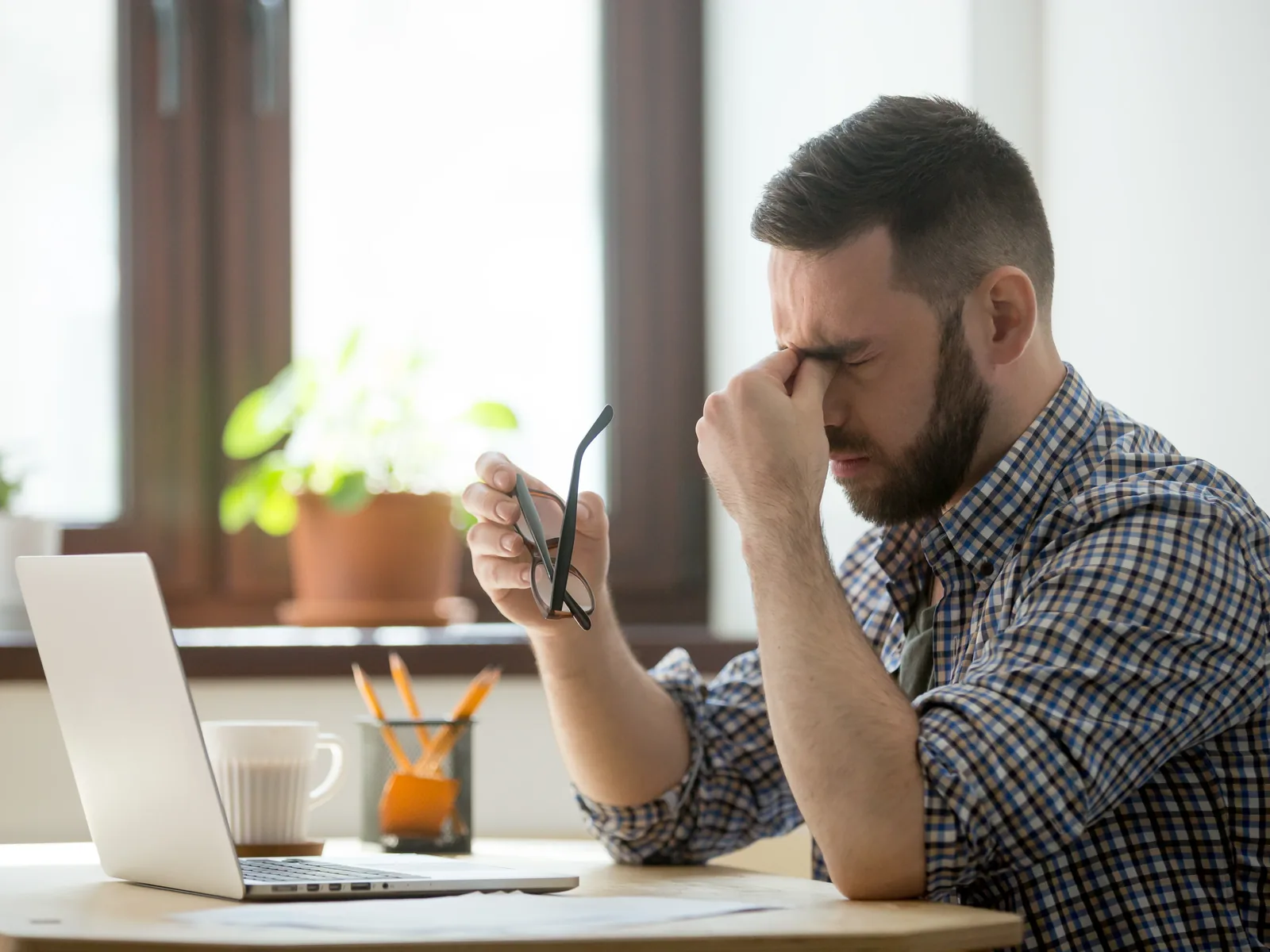 Stressed man rubbing bridge of nose while working at laptop