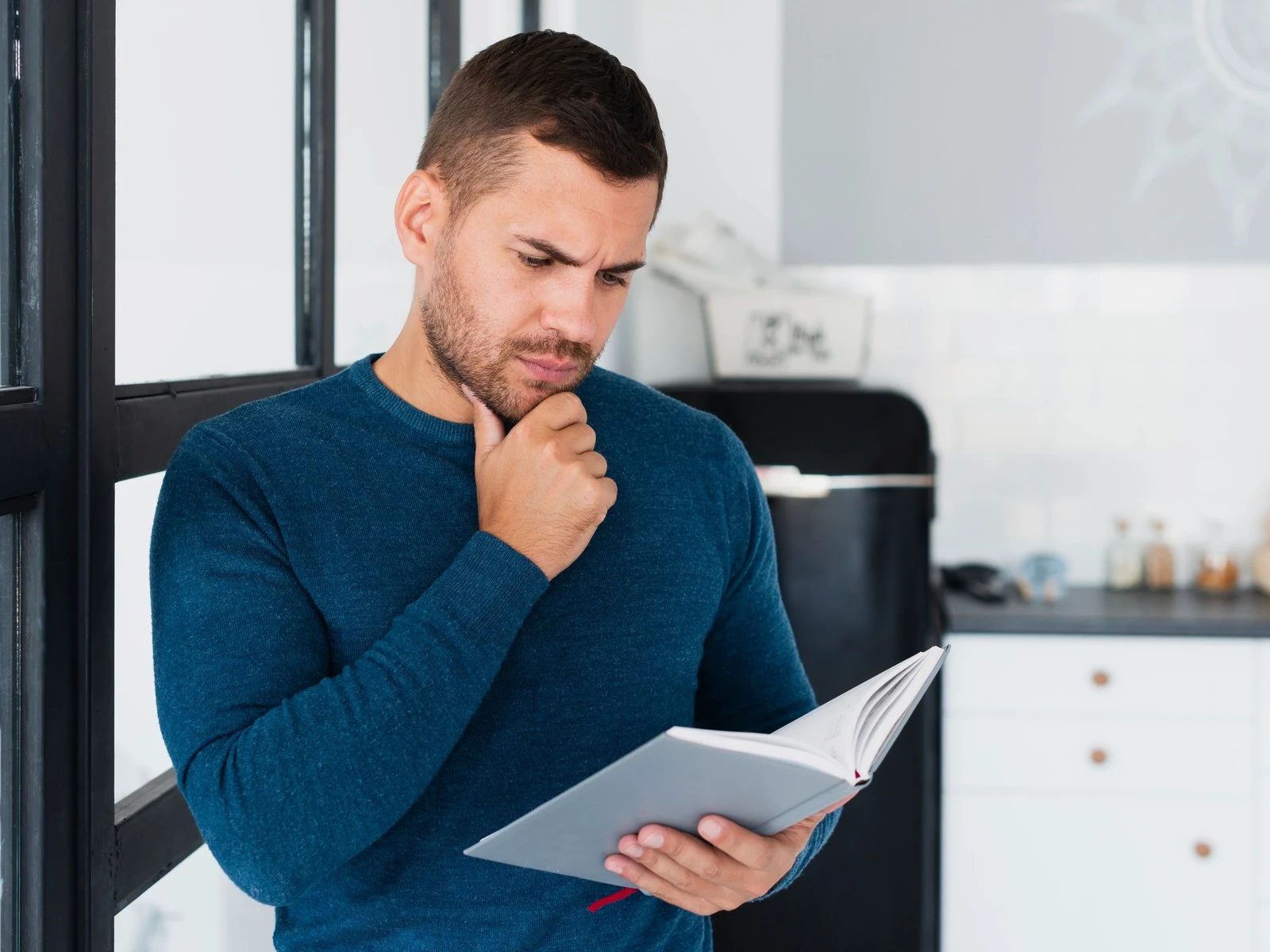 Thoughtful man reading notebook with hand on chin at home