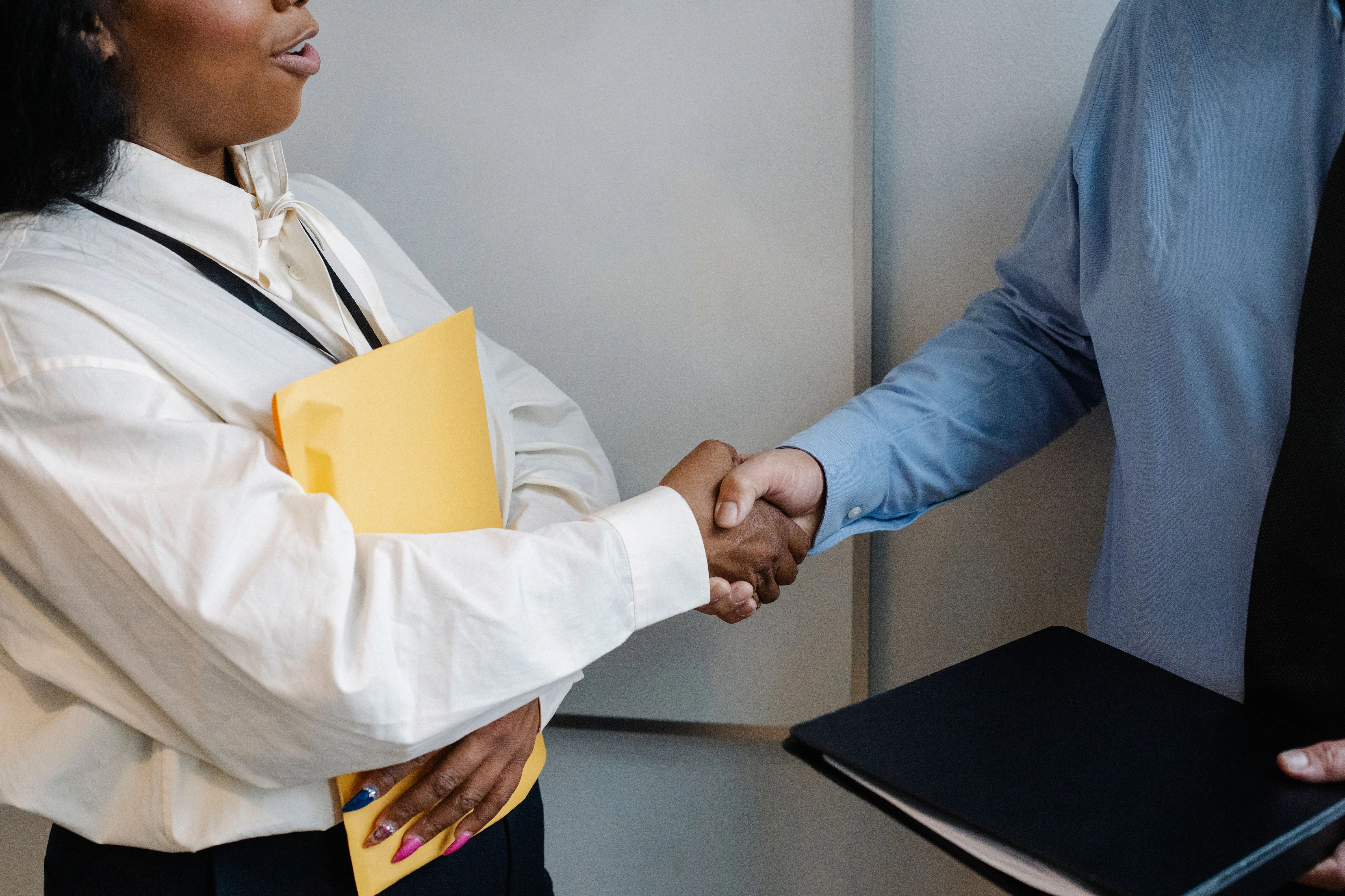 women smiling holding envelope with insurance paperwork shaking hands with private insurance broker